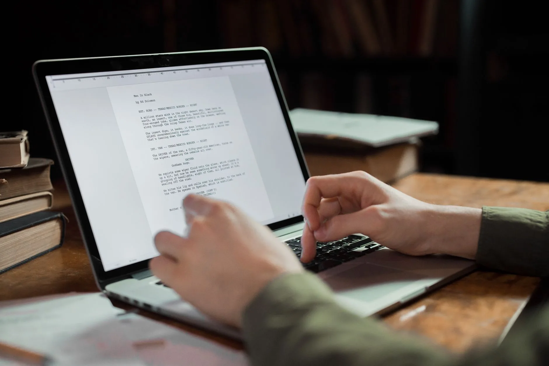 Penulis mengetik naskah di laptop dikelilingi tumpukan buku